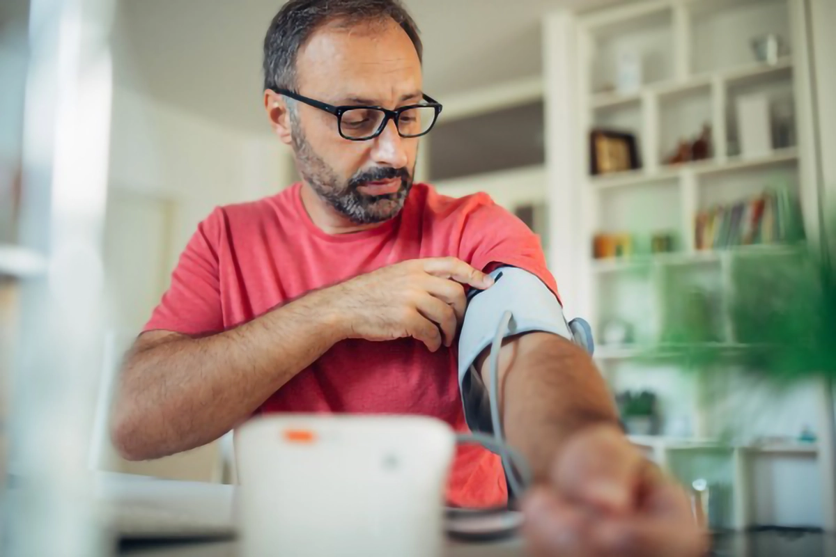 Image shows a man with a blood preasure cuff on his left arm checking his blood pressure at home
